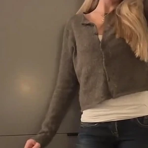 Mjuk grå kofta med knappar - Säljer en mysig jättefin grå kofta med knappar framtill. Koftan har en enkel, rak passform och är tillverkad i ett fluffigt, mjukt material som ger en avslappnad look. Perfekt att slänga över ett linne eller t-shirt för en chill stil. Brun/beige/grå färg 