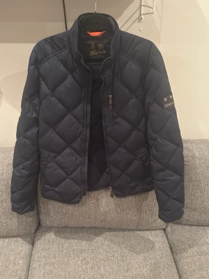  Morris dunjacka  - Snygg mörkblå dunjacka från Morris med quiltat mönster och klassisk patch på ärmen. Jackan har en stilren design och är tillverkad i ett tåligt material som håller värmen under kalla dagar. Perfekt för dig som vill ha en tidlös och trendig look.