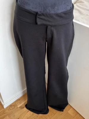 Svarta bootcut mjukisbyxor - Säljer ett par svarta mjukisbyxor med bootcut-modell och bred linning. Byxorna är i mjukt och stretchigt material, perfekta för chill dagar. Passformen är relaxed och de har ingen synlig logga eller fickor.
