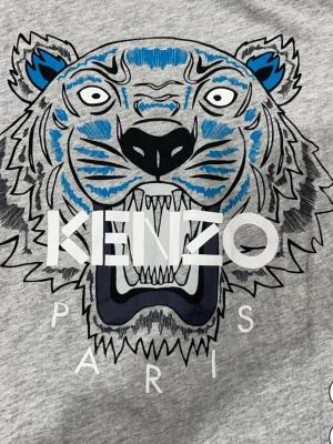 Grå Kenzo t-shirt med tigertryck - Snygg grå t-shirt från Kenzo med ikoniskt tigertryck i blått, svart och vitt. Tröjan har en pyttelitet håll vid armhålan men syns knappt 