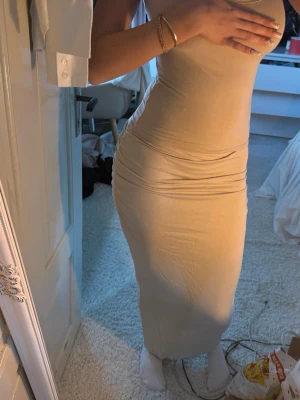 Beige långkjol - Snygg beige långkjol med slim passform och ärmlös design. Kjolen har en enkel, stilren look och är gjord i mjukt bomullsmaterial som sitter tajt mot kroppen. Perfekt för dig som gillar minimalistisk stil och vill ha något bekvämt men ändå trendigt. I storlek m men passar s. 