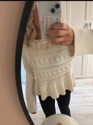 Vit stickad tröja med volangkant - Säljer en krämvit stickad tröja med volangkant nedtill och snyggt strukturmönster. Tröjan har långa ärmar och rund halsringning. Perfekt för dig som gillar en söt och trendig look.