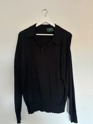 Svart långärmad pikétröja Alan Plaine - Klassisk svart långärmad pikétröja från Ralph Lauren. Tröjan har krage, knäppning vid halsen och ribbade muddar vid ärmslut och nederkant. Perfekt för en stilren och enkel look.