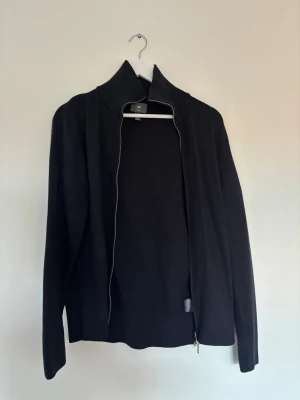 Marin blå ziptröja från H&M - Säljer en marinblå ziptröja från H&M med hög krage och långa ärmar. Tröjan har en enkel och stilren design med dragkedja framtill. Perfekt att slänga på sig över en t-shirt för en clean look.