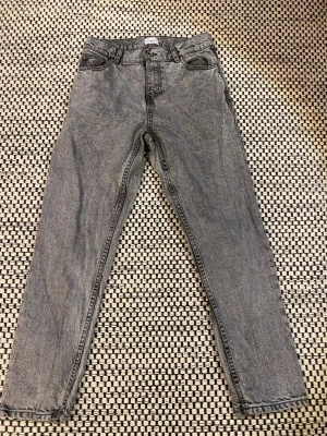 Grå raka jeans - Säljer ett par grå tvättade jeans med rak passform och klassisk femficksdesign. Jeansen har hög midja och är tillverkade i ett robust denimtyg. Perfekta för en avslappnad och trendig look.  Det var ett hål i den högra fickan men det är lagat.