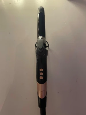 Svart locktång med guldiga detaljer - En stilren locktång i svart med guldiga detaljer och tre knappar på handtaget. Tången har ett klassiskt klämgrepp och är tillverkad i plast och metall. Perfekt för att fixa snygga lockar snabbt och enkelt.