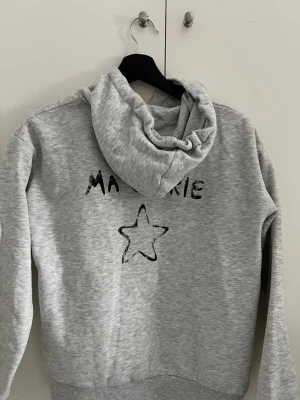 Ma Chérie hoodie från Gina Tricot - Säljer en ljusgrå hoodie med huva och dragsko. På bröstet och ryggen står det 'MA CHERIE' och en  stjärna tryckt i svart. Hoodien har ribbade muddar vid ärmslut och nederkant. Ena metallbiten har gått av på snöret men ser fortfarande bra ut! 