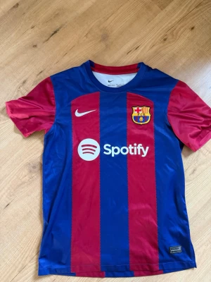 Barcelona fotbollströja hemma 23/24 - Snygg FC Barcelona matchtröja från Nike i blått och rött med klubbmärke, Spotify-logga och UNHCR-tryck. Tröjan har korta ärmar, rund hals och är tillverkad i ett lätt, ventilerande material som passar perfekt till fotbollsträning eller match. Pris kan diskuteras vid snabb affär.