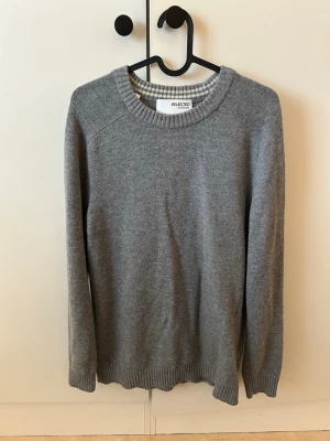 Grå stickad tröja Selected Homme - En grå stickad tröja från Selected Homme med rund halsringning och ribbade muddar vid ärmslut och nederkant.