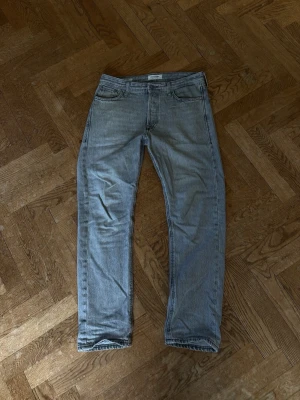 Gråa raka jeans W27/L30 - Säljer ett par ljusblå jeans från Jack n Jones med klassisk femficksdesign och raka ben. Jeansen har subtila slitningar och är tillverkade i denim med tydlig struktur. Perfekta för en avslappnad och stilren look.
