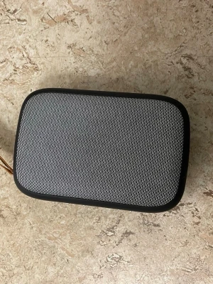 Svart och grå bärbar högtalare - Snygg bärbar högtalare i svart plast med grått metallgaller på framsidan. Högtalaren har en rektangulär form med rundade hörn och en praktisk brun tygrem för enkel transport. Perfekt för att ta med sig musiken överallt.