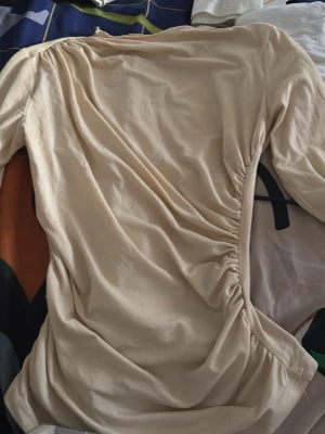 Beige omlottblus med rynkdetalj - Trendig beige blus med omlott-design och snygga rynkdetaljer längs sidan. Tillverkad i ett mjukt, lätt material som ger en skön känsla. Perfekt att styla med jeans eller kjol för en chic look.