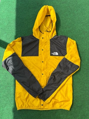 Gul och svart vindjacka från The North Face - Snygg gul och svart vindjacka från The North Face med huva och tryckknappar framtill. Funkar bra under kalla sommarkvällar och senare under höst 🍂 super bra skick. PRIS kan diskuteras  STORLEK är S men passar M också beroende på hur man vill att den sitter 