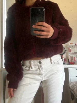 Vinröd pälsjacka från Hollies burgundy  - Sjukt snygg vinröd pälsjacka från Hollies i mjuk kaninpäls (etisk restprodukt) med ribbade muddar och krage. Jackan har dragkedja framtill och fodrad insida i polyester. 
