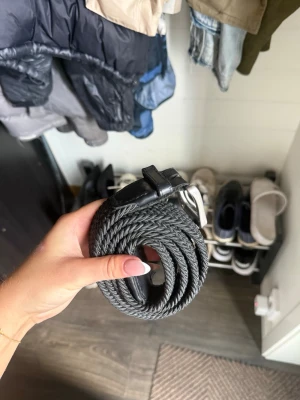 Svart flätat bälte med silverfärgat spänne - Snyggt svart flätat bälte med ett stilrent silverfärgat metallspänne och detaljer i svart läderimitation. Perfekt för att ge din outfit en clean och modern touch. Passar till både jeans och kostymbyxor.