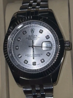 Rollie Datejust - Snygg Datejust med silverfärgad urtavla och länkarmband i metall. Urtavlan har glittriga stenar som timmarkeringar och datumfönster vid klockan tre. Klassisk räfflad bezel och elegant design som sticker ut.