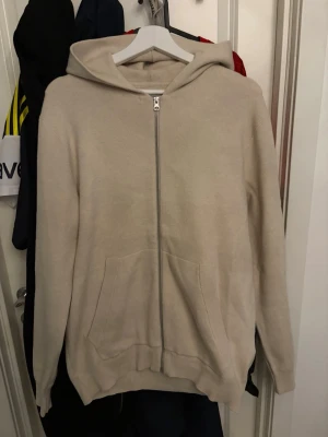 Beige hoodie från Jack & Jones - Snygg beige hoodie från Jack & Jones Core med dragkedja framtill och två stora fickor. Hoodien har en klassisk huva och är tillverkad i mjukt material, perfekt för en avslappnad stil. Passar till det mesta och är enkel att matcha med andra plagg.