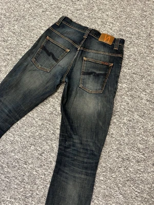 Mörkblå jeans från Nudie Jeans - Snygga mörkblå jeans från Nudie Jeans med klassisk femficksdesign och kontrastsömmar. Jeansen har en lätt tvättad look och läderpatch bak i midjan. Perfekta för en avslappnad stil. Hör av dig vid minsta fråga 👍