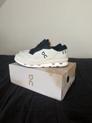 On Running sneakers - Snygga sneakers från On i vitt och svart med låg profil och modern design. Skorna har ventilerande meshmaterial, svarta snören och detaljer samt On-logga på sidan. Sulan är vit med On's karakteristiska dämpning för extra komfort.