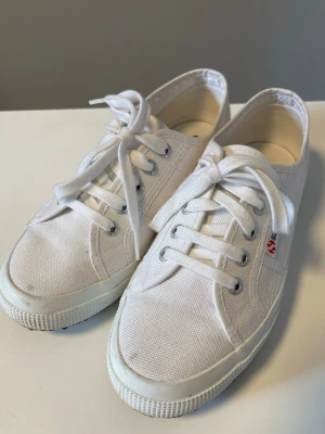 Vita Superga sneakers - Säljer ett par klassiska vita Superga sneakers i canvas med rund tå och vita snören. (2750-Cotu Classic 901 White). Skorna har en låg profil och gummisula som ger en clean och tidlös look. Perfekta för dig som gillar enkel och stilren design. Nypris: 849kr. 