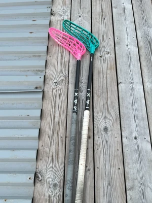 Två innebandyklubbor från Unihoc  - Säljer två innebandyklubbor från Unihoc , en med rosa blad och en med turkost blad. Båda har svart skaft, där den ena har vitt lindat grepp. Perfekt för dig som vill spela innebandy med stil. Materialet är plast och komposit.