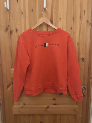 Röd sweatshirt från Marine Sports -  röd sweatshirt från Marine Sports med tryckt logga på bröstet. Tröjan har rund halsringning, långa ärmar och ribbade muddar vid ärmslut och nederkant. Perfekt för en avslappnad och sportig stil. Storlek M