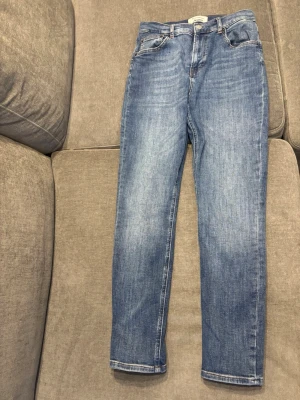 Blå raka jeans från Reformation - Säljer ett par klassiska blå skinny jeans från Reformation med hög midja. Jeansen har rak passform, fem fickor och en snygg tvättad look. De är tillverkade i denim och passar perfekt för en avslappnad och trendig stil.