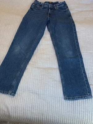 Blå raka jeans i storlek 152 Jack and Jones - Klassiska blå jeans med rak passform och justerbar midja. Jeansen har fem fickor och kontrastsömmar. Perfekta för en avslappnad och tidlös look. Tillverkade i slitstarkt denimtyg.jack and Jones