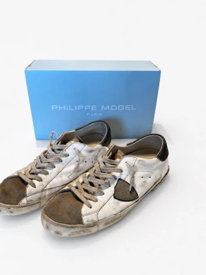 Philippe Model vita sneakers - Sneakers från Philippe Model i vitt läder med svarta detaljer och grå snörning. Klassisk låg modell med svart häl och märke på sidan. Yttersula i gummi med vågmönster. Snygg streetstil med vintagekänsla.