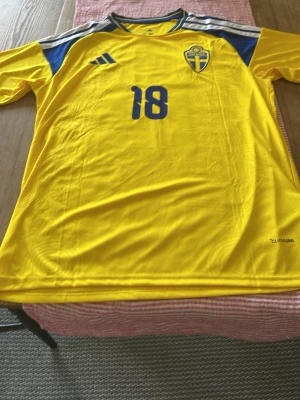 Svensk landslagströja  nr 18 AYARI - Helt ny. Gul och blå fotbollströja från Adidas med Sveriges landslagsemblem på bröstet och nummer 18 både fram och bak. 