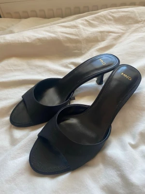Svarta klackskor från MNG - Stilrena svarta slip-in klackar från MANGO med öppen tå och bred rem över foten. Dem är helt oanvända med lappen kvar och säljer dem för att dem inte passar mig🥰(köpte dem för 430kr).  