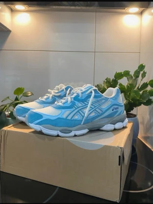 ASICS blå och vita sneakers - Snygga sneakers från ASICS i blått och vitt med mesh- och syntetmaterial. Skorna har klassisk låg profil, vita snören och en robust sula som ger bra komfort. Perfekt för dig som gillar sportig stil och vill ha något fräscht till vardags.