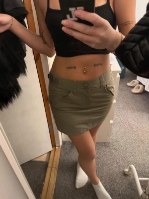 Olivgrön kortkjol med fickor - Säljer en olivgrön kortkjol med två stora fickor framtill och knappstängning. Kjolen har en enkel och clean design som är lätt att matcha med olika toppar. Perfekt för dig som gillar en avslappnad och cool stil.