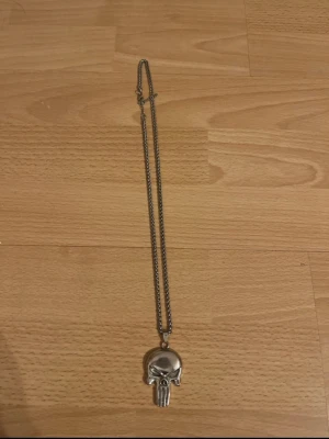 Halsband med dödskallehänge i silverfärg - Coolt halsband med ett detaljerat dödskallehänge i silverfärgad metall. Kedjan är tunn och har en klassisk länkdesign. Perfekt accessoar för dig som gillar edgy och unika smycken.