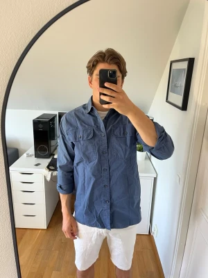 Blå overshirt med fickor från Morris - Snygg blå overshirt i bomull med två bröstfickor och knappar hela vägen. Skjortan har klassisk krage och lång ärm. Skjortan är ifrån Morris. Hör gärna av dig vid frågor!