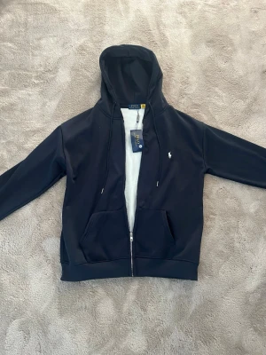 hoodie Polo Ralph Lauren - Mörkblå hoodie med dragkedja från Polo Ralph Lauren. Storlek XL men passar L