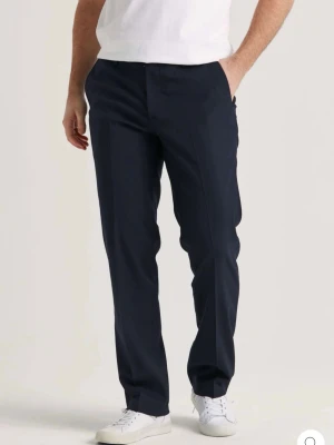 Mörk blåa raka kostymbyxor - Snygga mörk blåa kostymbyxor med rak passform och klassisk design. Byxorna har hällor för bälte och två fickor bak. Perfekta för en stilren look och passar till skjorta eller t-shirt.