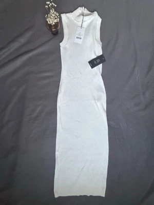 HELT NY Beige ribbad långklänning NA-KD - Snygg beige ribbad långklänning från NA-KD med ärmlös design och hög hals. Klänningen har en figurnära passform och är tillverkad i mjuk bomullsmix som ger en bekväm känsla. Perfekt för dig som gillar stilrena och minimalistiska plagg. Aldrig använd!🥰