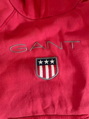 Röd Gant Hoodie -  Detta är en röd Gant hoodie för både män och kvinnor. Den har varit använd några gånger, färgen är lite urtvättad, fast ser fortfarande bra ut. 
