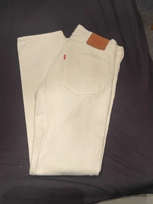 Beiga Levi's jeans med rak passform - Säljer ett par snygga beiga jeans från Levi's med klassisk rak passform.501:or Jeansen har fem fickor, Levi's ikoniska läderpatch bak och röd logotagg på bakfickan. Perfekta för en clean och stilren look.
