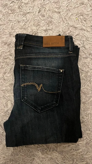 Jeans från Mos Mosh - Snygga mörkblå jeans från Mos Mosh med dekorativa nitar på fickan och guldfärgad söm på bakfickan. 