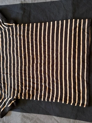 Randig t-shirt från Forever 21 - Snygg svart t-shirt med smala beigea ränder från Forever 21. Modellen är klassisk med korta ärmar och rund hals. Tillverkad i mjuk bomull som känns skön mot huden. Perfekt för en avslappnad och trendig look.