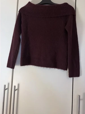 Vinröd stickad tröja från Gina Tricot - Mysig vinröd stickad tröja med lång ärm och bred, nedvikt krage. Tröjan har ribbstickade muddar vid ärmslut och nederkant. Perfekt för kyliga dagar och enkel att matcha med jeans eller kjol.
