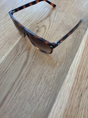 Bruna solglasögon i wayfarer-stil - Snygga solglasögon med brunmelerat sköldpaddsmönster och klassisk wayfarer-form. Glasen är bruna och bågarna är tillverkade i plast. Perfekta för att ge din outfit en cool touch i solen.