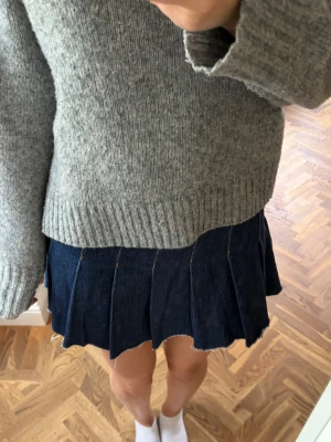 Mörkblå plisserad jeanskjol - Snygg mörkblå kort jeanskjol med plisserad design och synliga sömmar. Kjolen har en klassisk denimlook och passar perfekt till en stickad tröja eller t-shirt. Enkel att styla för en trendig vardagsoutfit.