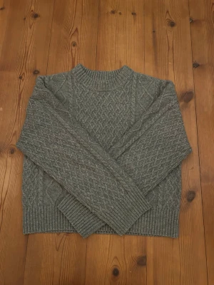 Grå kabelstickad tröja från H&M - Säljer en grå kabelstickad tröja från H&M i storlek XS. Tröjan har rund halsringning, ribbade muddar.