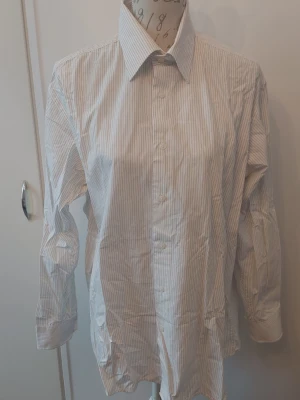 Vit randig skjorta från Shirt Industry - Klassisk vit skjorta med tunna svarta ränder från Shirt Industry. Skjortan har lång ärm, knappar framtill och en stilren krage. 