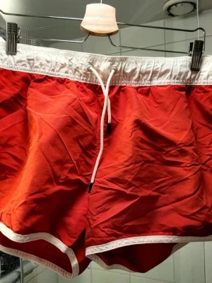 Röda badbyxor med vit kant - Snygga röda badbyxor från G-Star med vit resår och dragsko i midjan. De har vita detaljer längs kanterna och en liten logga på benet. Perfekta för stranden eller poolen, klassisk modell med sportig känsla.