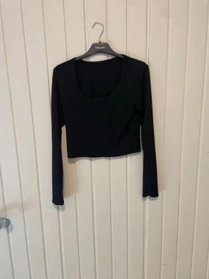 Svart ribbad croppad topp KappAhl - Svart långärmad croppad topp från KappAhl med ribbad struktur och rundad urringning. Perfekt att styla med jeans eller kjol för en trendig look.
