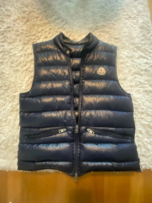 Moncler Väst - Hej, säljer denna mörkblåa Moncler väst i ytters skick. NFC scannen funkar, bara att be om video ifall ni vill se. Inga synliga skador alls. Har haft den i 1 år. Storlek S/small. Bara att höra av sig vid frågor.